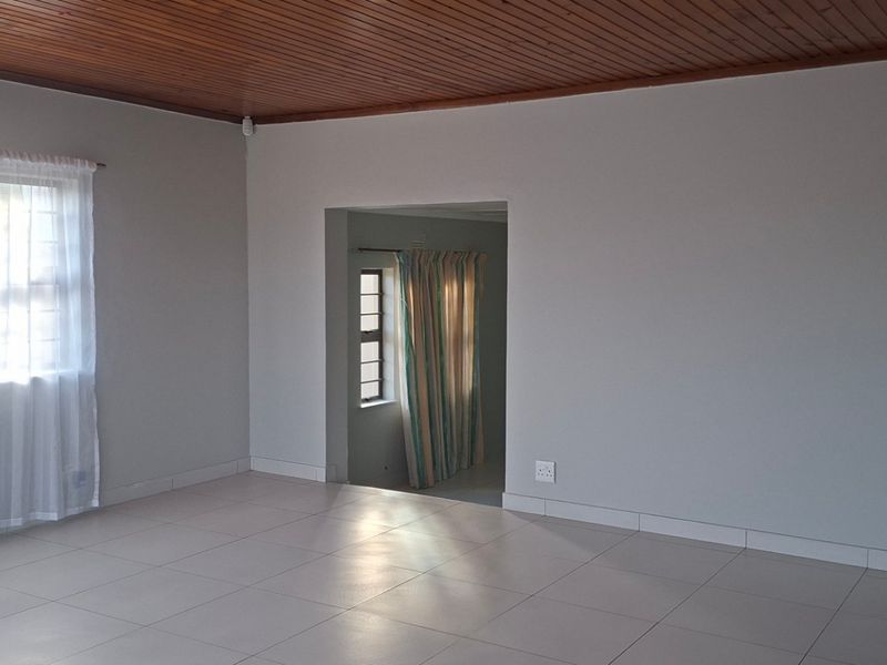 Spacious living area featuring neutral tiled flooring, a warm timber-clad ceiling, and a wall-mounted air conditioning unit.