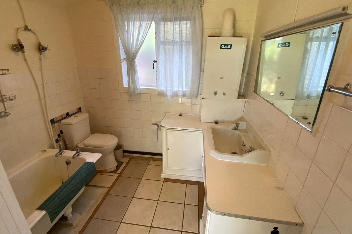 A functional bathroom featuring a bathtub, toilet, vanity basin, and a wall-mounted gas water heater, finished with tiled walls and flooring.