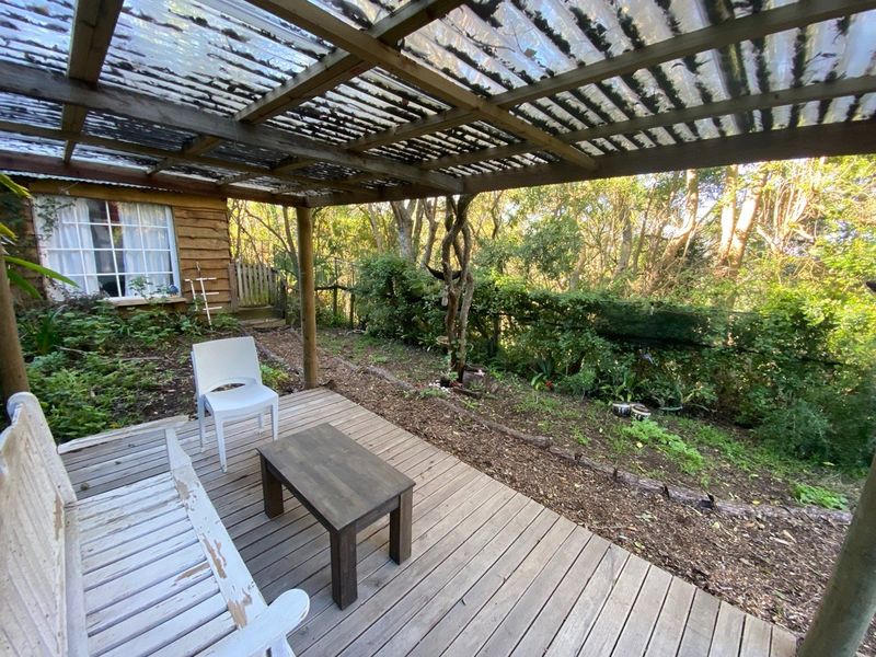 A rustic outdoor timber deck featuring a corrugated plastic roof pergola, overlooking a natural garden setting.