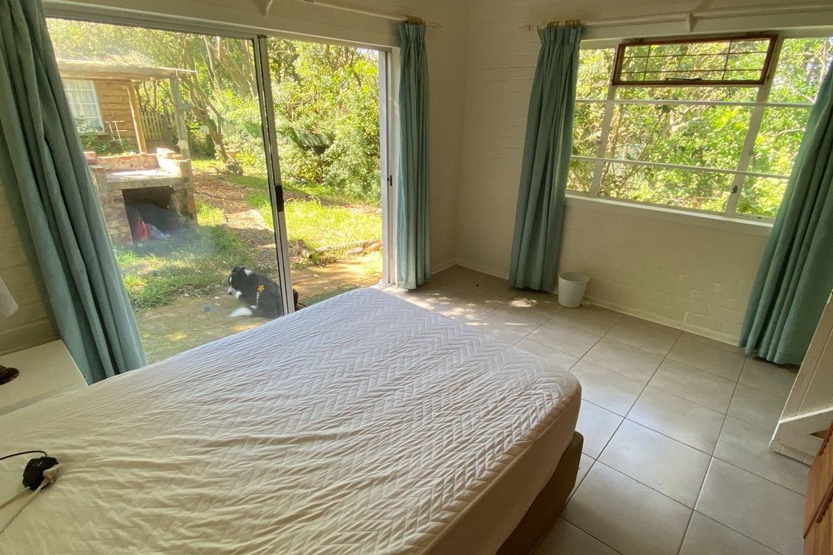 A bright bedroom featuring tiled flooring, timber wall paneling, and large sliding glass doors providing direct access to the garden.
