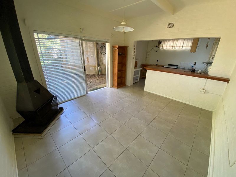 Open plan living area featuring a freestanding fireplace, tiled floors, and a breakfast bar connecting to the kitchen, with direct access to the exterior.