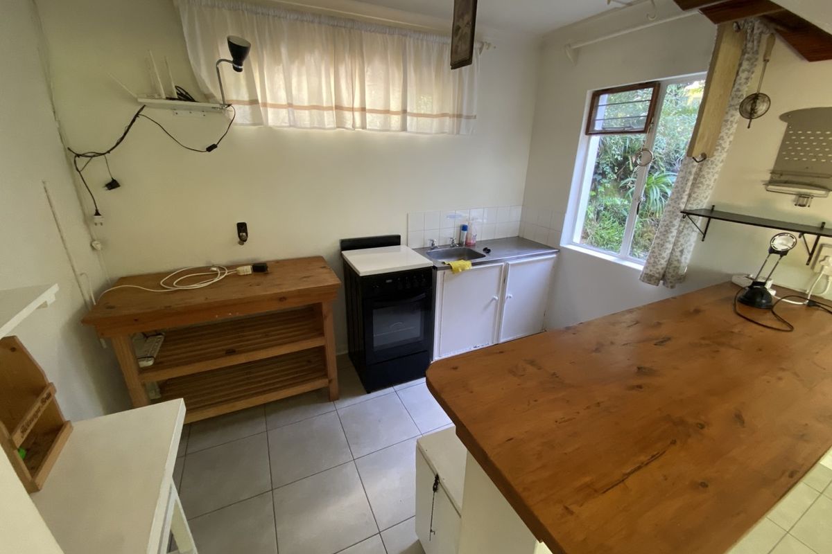 A compact kitchen area featuring tiled flooring, a stainless steel sink, and a freestanding stove, offering a functional space with potential for modernization.