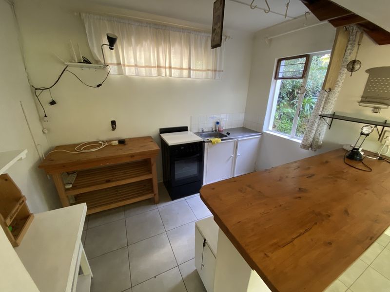A compact kitchen area featuring tiled flooring, a stainless steel sink, and a freestanding stove, offering a functional space with potential for modernization.