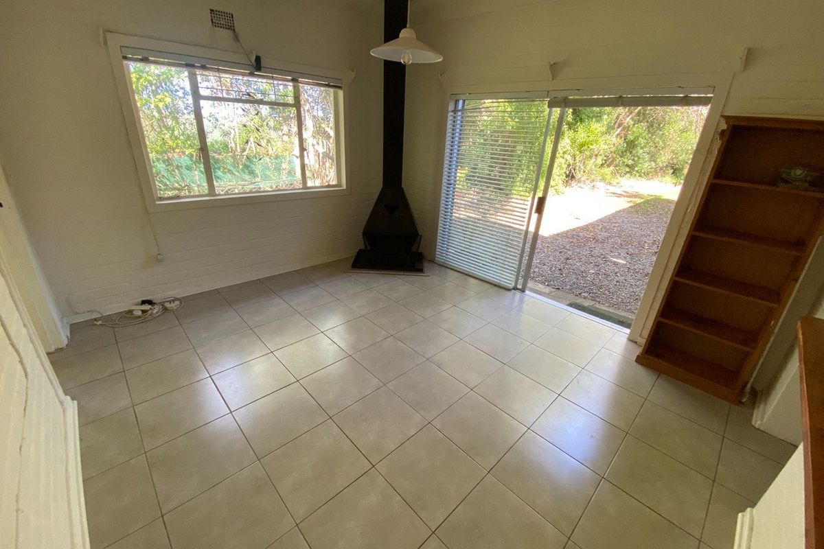 An empty living room featuring tiled flooring, a freestanding fireplace, and large sliding glass doors providing access to the outdoor area.