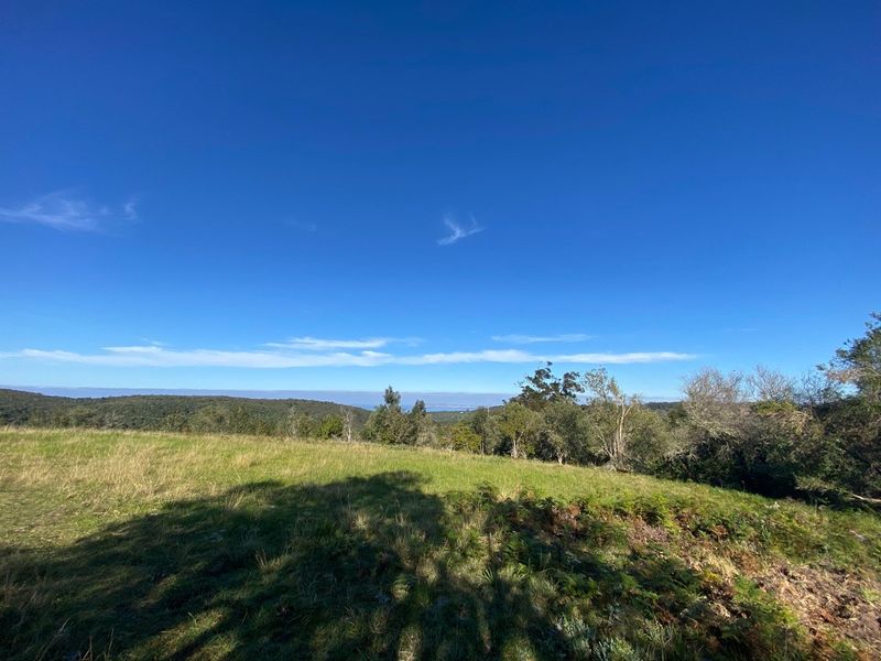 A scenic, elevated view of the surrounding natural landscape, featuring open grassy fields and distant hills under a clear blue sky.