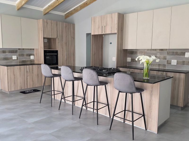 Modern kitchen featuring light wood-tone cabinetry, dark stone countertops, a central island with gas hob, and exposed timber ceiling beams.