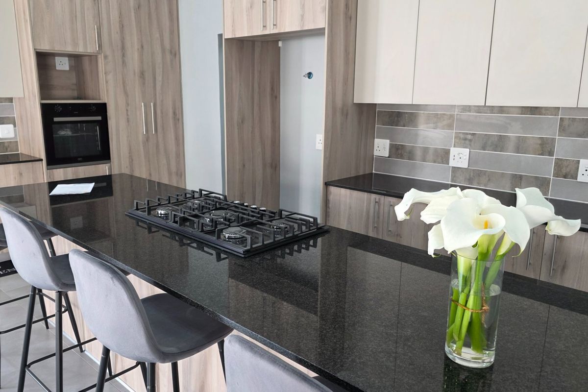 Modern kitchen featuring sleek laminate cabinetry, granite countertops, a built-in oven, and a gas hob, offering a clean and functional cooking space.
