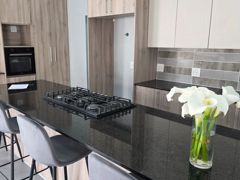 Modern kitchen featuring sleek laminate cabinetry, granite countertops, a built-in oven, and a gas hob, offering a clean and functional cooking space.