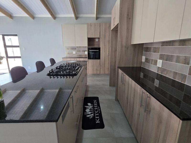 Modern kitchen featuring sleek cabinetry, granite countertops, a central island with a gas hob, and exposed timber ceiling beams.