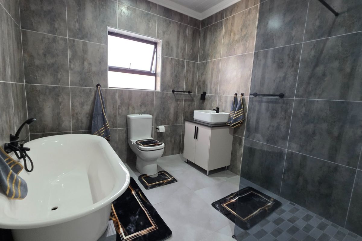 Modern bathroom featuring a freestanding bathtub, walk-in shower with glass screen, vessel sink on a vanity cabinet, and contemporary grey wall tiling.