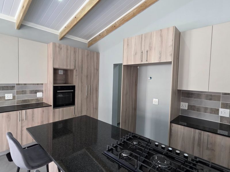 Modern kitchen featuring granite countertops, built-in oven, gas hob, and light wood-finish cabinetry with exposed timber ceiling beams.