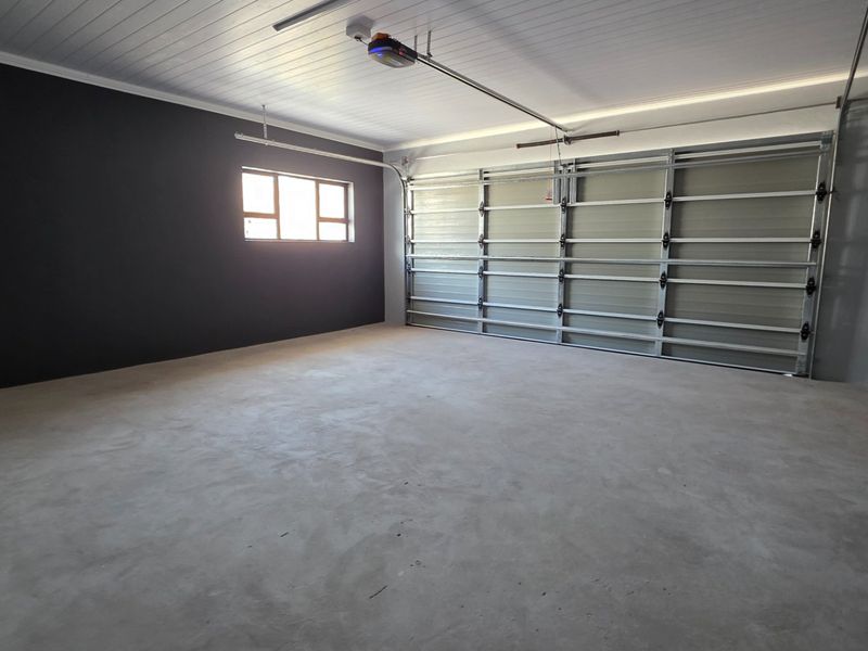 A clean, spacious double garage featuring concrete flooring, a white tongue and groove ceiling, and an automated sectional garage door.