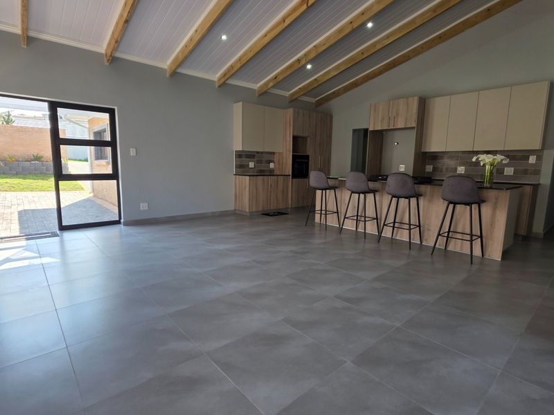 Spacious open-plan living area featuring modern kitchen cabinetry, a central island, exposed timber ceiling beams, and large glass doors opening to the garden.