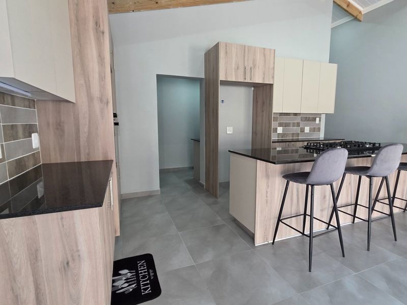 Modern kitchen featuring light wood cabinetry, dark stone countertops, a gas hob, and tiled flooring with an open-plan layout and exposed timber beams.