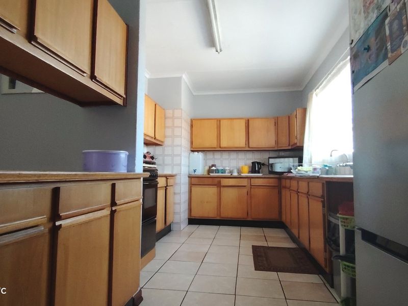 A functional kitchen featuring wooden cabinetry, tiled backsplash, and tiled flooring, offering a classic layout with potential for modern updates.