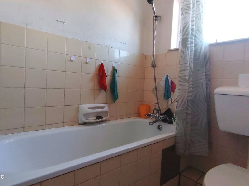A dated bathroom featuring a standard bathtub with shower mixer, toilet, and tiled walls. The space requires cosmetic updates and maintenance to improve its condition.