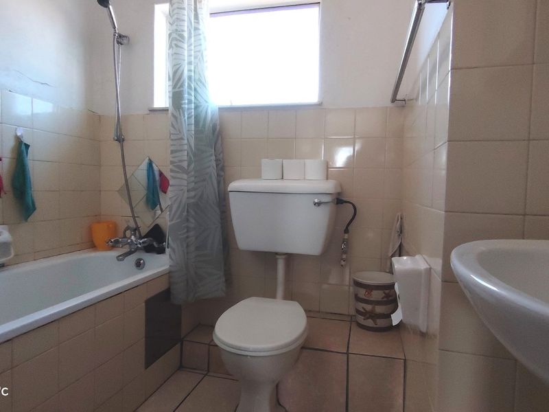 A dated bathroom featuring a standard bathtub, toilet, and washbasin with original ceramic tiling throughout.