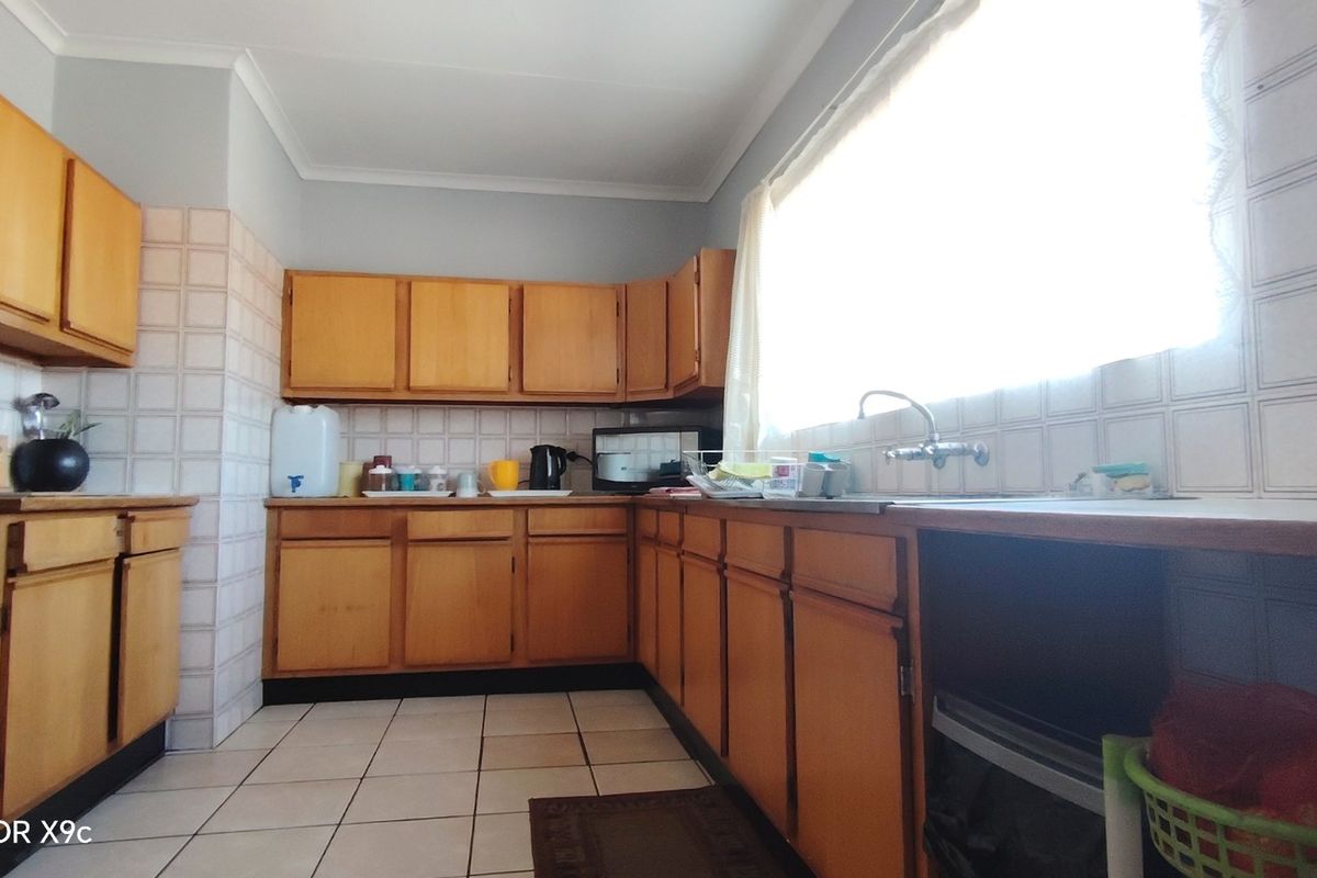 A functional kitchen featuring wooden cabinetry, tiled backsplash, and tiled flooring, offering a dated aesthetic with potential for modern renovation.