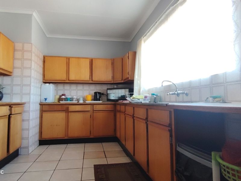 A functional kitchen featuring wooden cabinetry, tiled backsplash, and tiled flooring, offering a dated aesthetic with potential for modern renovation.
