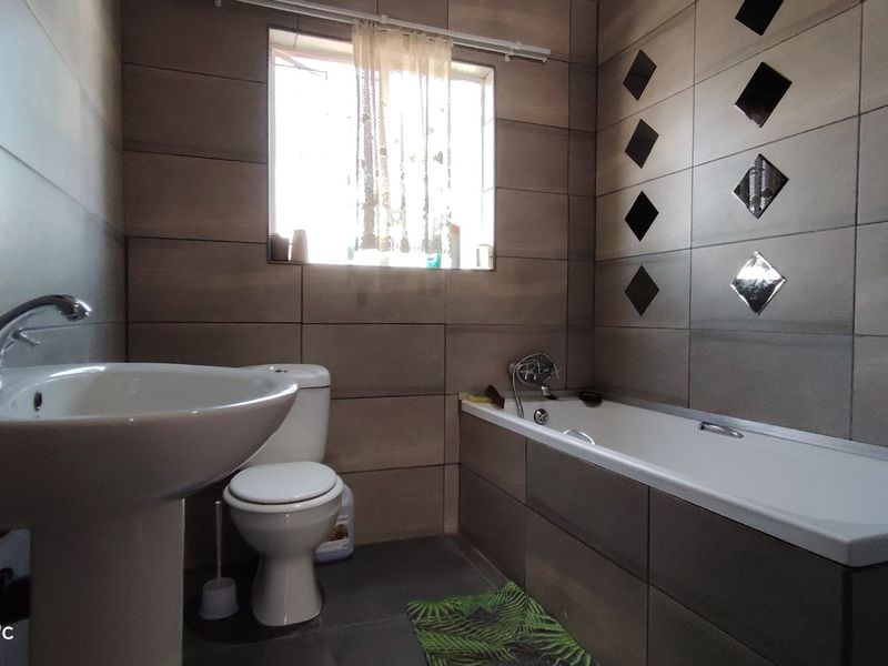 A functional bathroom featuring a pedestal basin, toilet, and bathtub with tiled walls and flooring.
