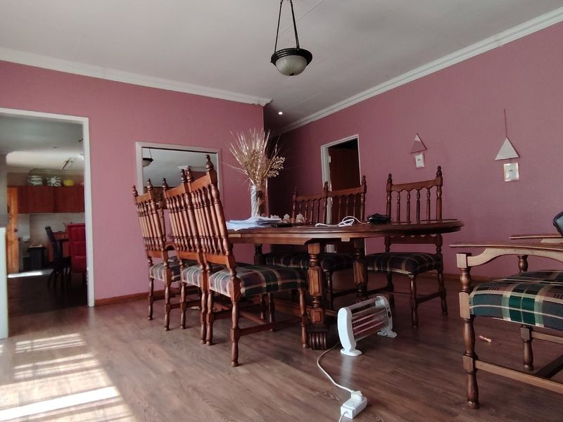 A dining room featuring laminate flooring, cove cornicing, and a pendant light fixture, with a view into the adjacent kitchen area.