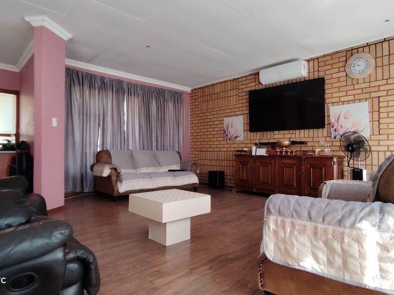 A spacious living room featuring an exposed brick feature wall, laminate flooring, and a split-system air conditioner.