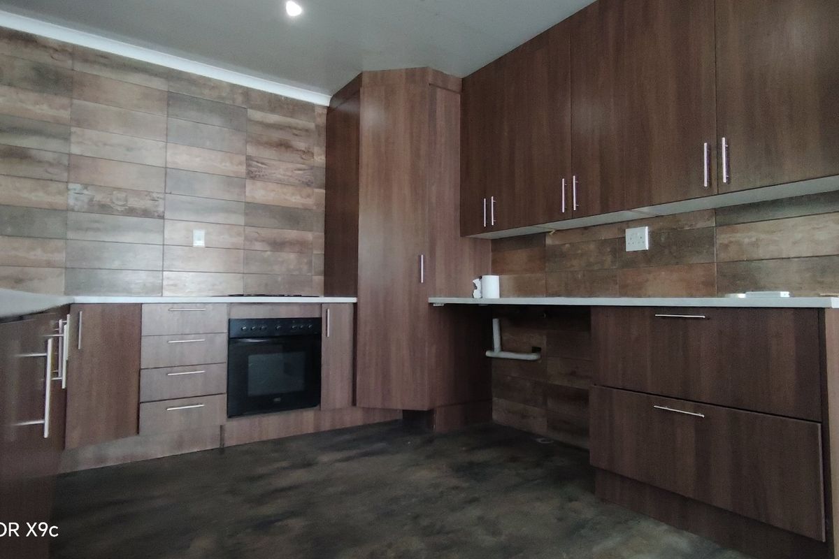 Modern kitchen featuring wood-look tile backsplash, dark laminate cabinetry, and a built-in oven with ample counter space.