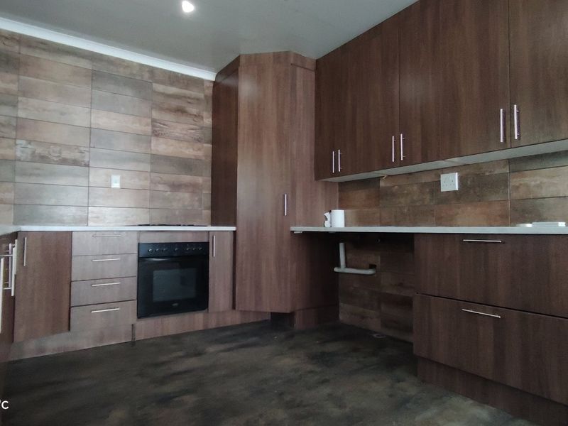 Modern kitchen featuring wood-look tile backsplash, dark laminate cabinetry, and a built-in oven with ample counter space.