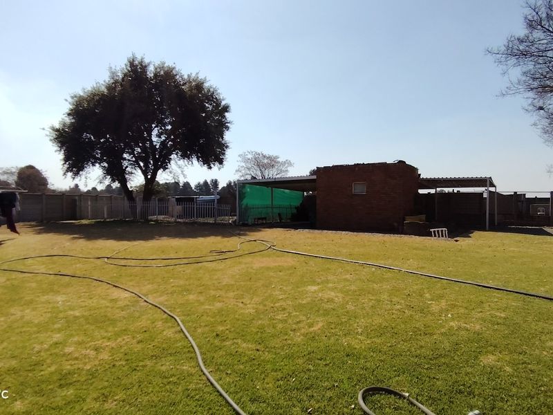 A spacious rear garden area featuring a brick outbuilding with a covered patio and perimeter precast concrete walling.