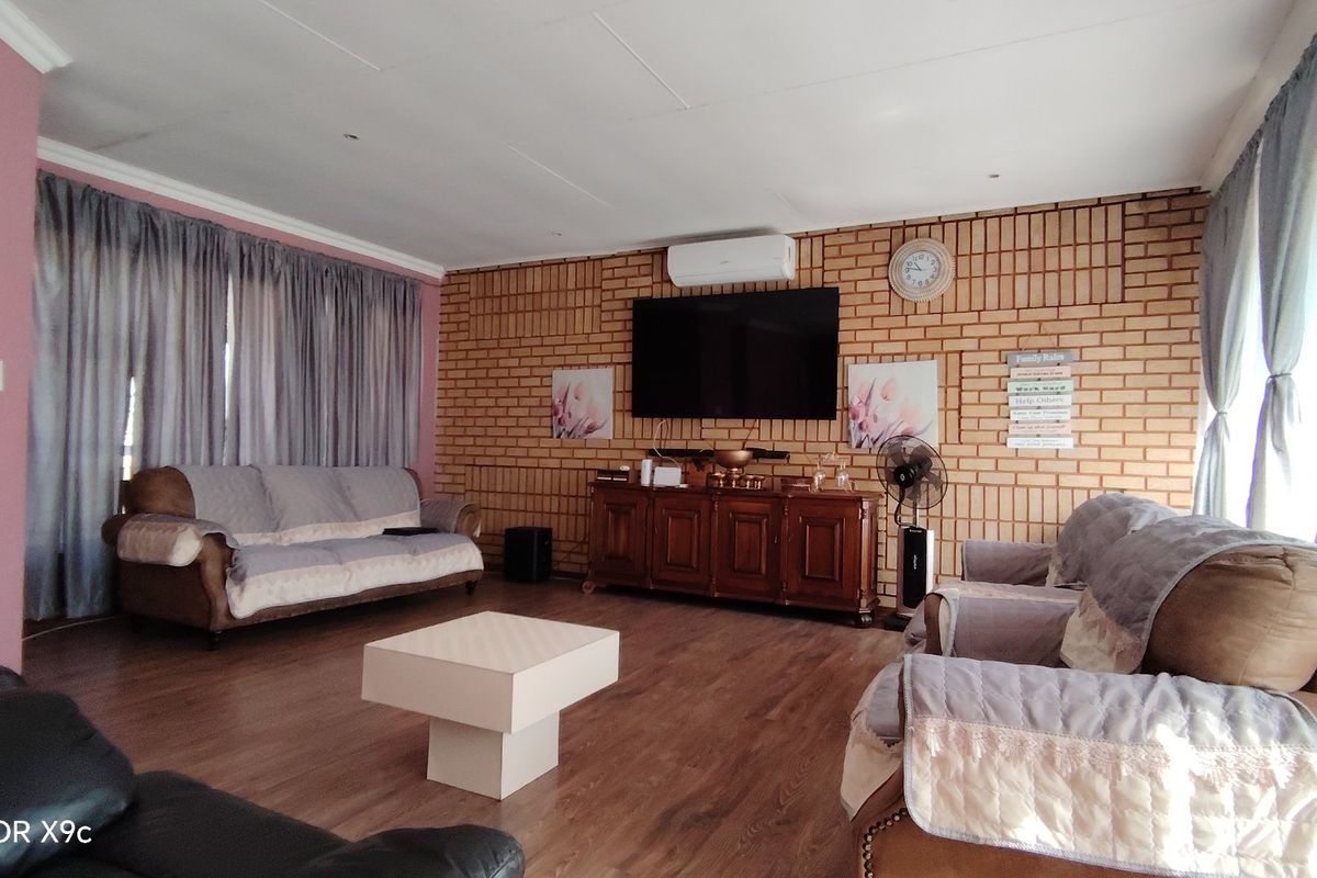 A spacious living room featuring an exposed brick feature wall, laminate flooring, and a wall-mounted air conditioning unit.
