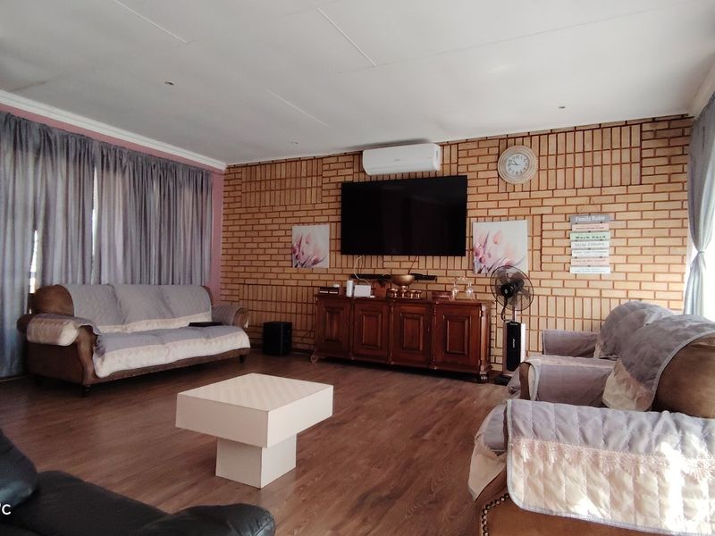 A spacious living room featuring an exposed brick feature wall, laminate flooring, and a wall-mounted air conditioning unit.
