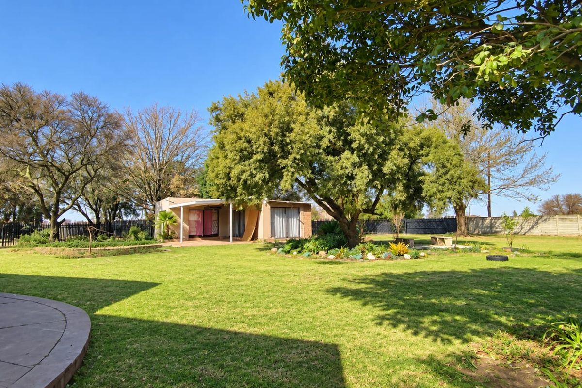 Spacious rear garden featuring a well-maintained lawn, mature trees, landscaped garden beds, and a concrete patio area.
