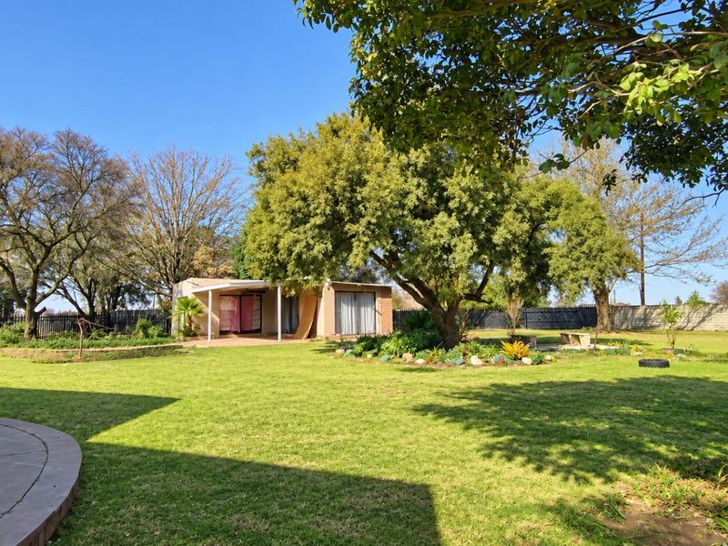 Spacious rear garden featuring a well-maintained lawn, mature trees, landscaped garden beds, and a concrete patio area.