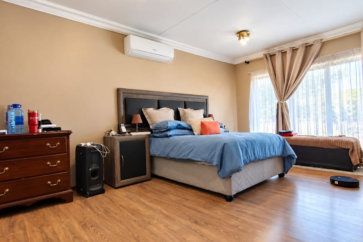 A spacious bedroom featuring laminate flooring, crown molding, and a wall-mounted air conditioning unit, with large windows providing natural light.