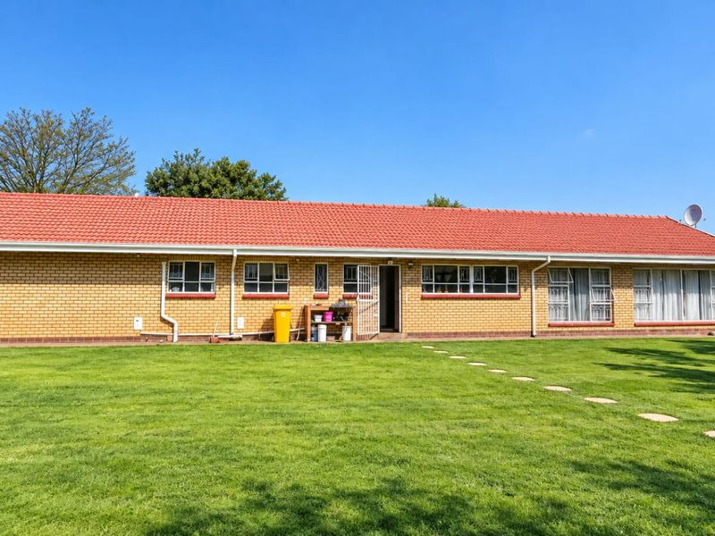 A well-maintained rear elevation of a brick farmhouse featuring a red tiled roof, large windows, and a spacious lawn area.