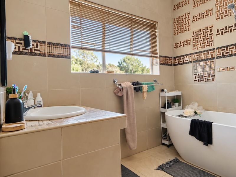A well-maintained bathroom featuring a modern freestanding bathtub, tiled vanity with basin, and decorative wall tiling.