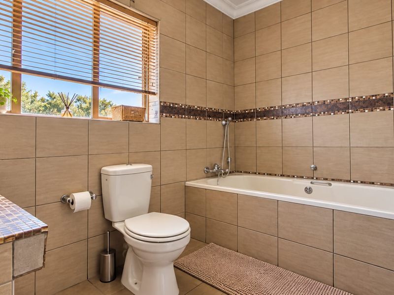 A well-maintained bathroom featuring neutral floor-to-ceiling tiling, a built-in vanity, a standard bathtub with shower attachment, and a window providing natural light.