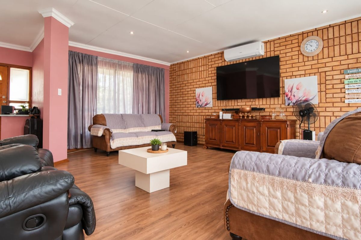 Spacious living room featuring an exposed brick feature wall, laminate flooring, and a split-system air conditioner, providing a comfortable and inviting atmosphere.