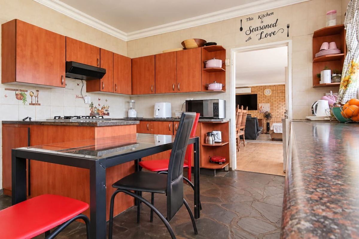 A functional kitchen featuring warm-toned laminate cabinetry, granite countertops, a gas hob with extractor fan, and durable stone flooring.