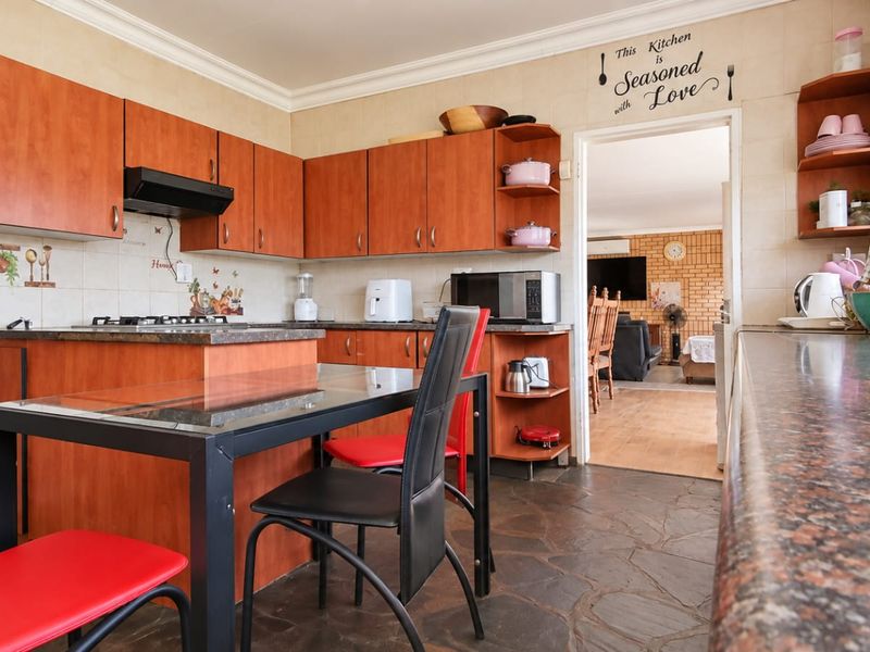 A functional kitchen featuring warm-toned laminate cabinetry, granite countertops, a gas hob with extractor fan, and durable stone flooring.