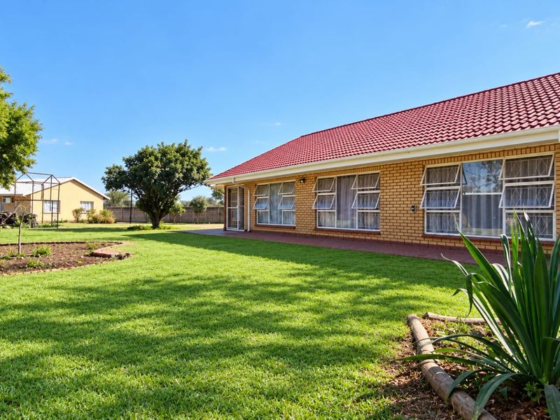 A well-maintained rear exterior view of a brick farmhouse featuring a red tiled roof, large windows, and a spacious, manicured lawn.