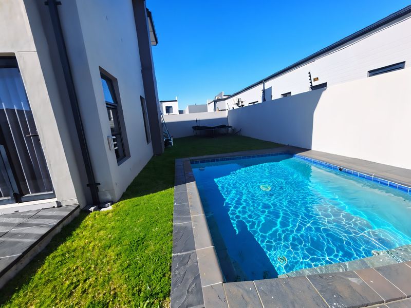 A well-maintained rear garden area featuring a modern swimming pool with stone coping, bordered by a high boundary wall with electric fencing.
