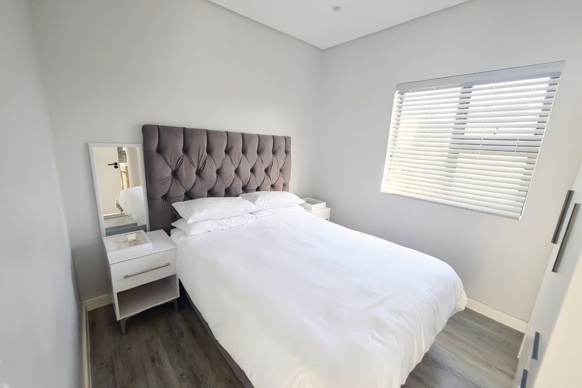 A modern, well-maintained bedroom featuring neutral walls, laminate flooring, recessed lighting, and fitted window blinds.