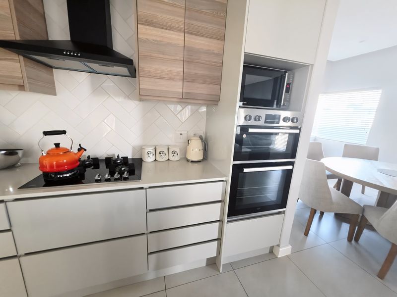 Modern kitchen featuring sleek cabinetry, stone countertops, a herringbone tile backsplash, and integrated appliances including a double oven and gas hob.