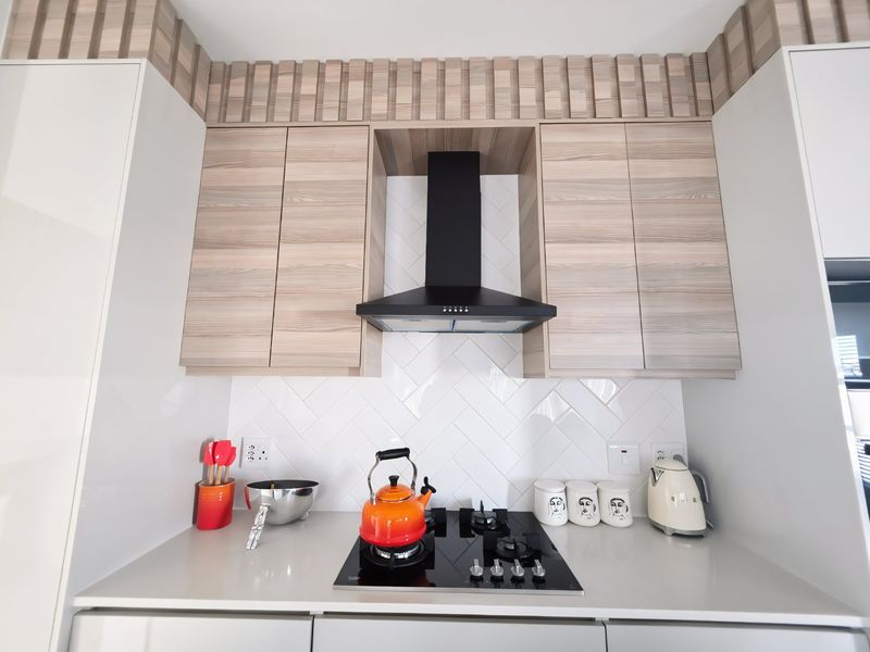 Modern kitchen featuring a sleek gas hob, black extractor fan, herringbone tiled backsplash, and contemporary wood-grain cabinetry with stone countertops.