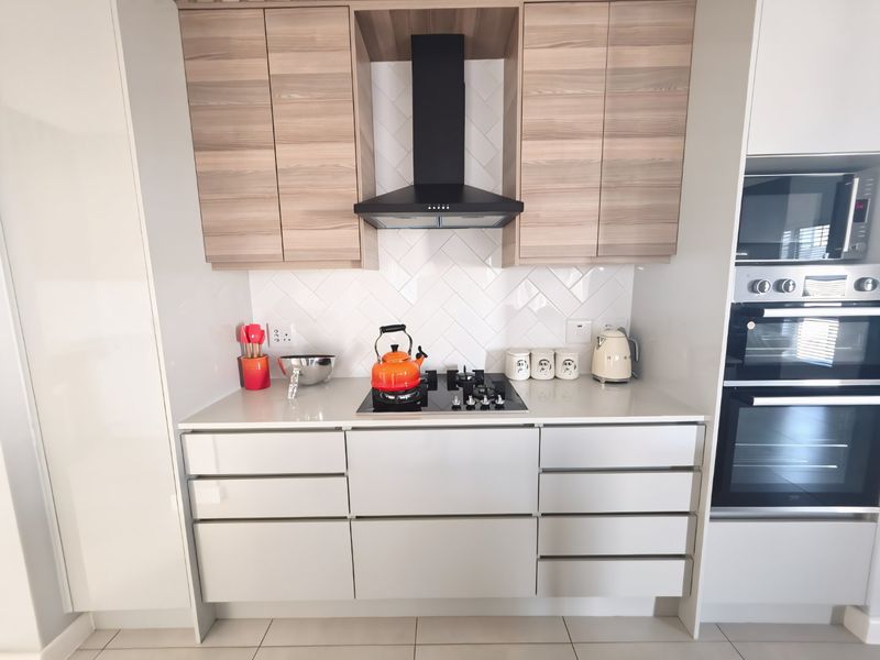 Modern kitchen featuring sleek handleless cabinetry, stone countertops, a herringbone tile backsplash, and integrated stainless steel appliances including a gas hob and double oven.