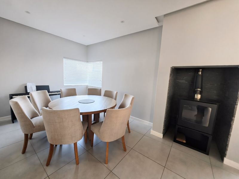 A bright dining room featuring large format floor tiles, recessed ceiling lighting, and a modern built-in fireplace with a dark stone surround.