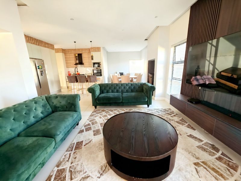 Spacious open-plan living area featuring a modern kitchen with built-in appliances, a dining space, and a contemporary lounge with a wood-paneled feature wall.
