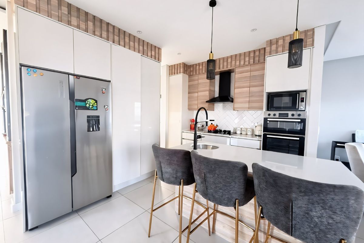 Modern kitchen featuring sleek white and wood-tone cabinetry, a central island with stone countertops, integrated appliances, and contemporary pendant lighting.