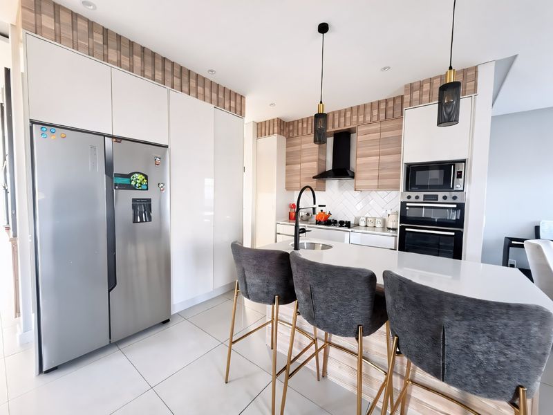 Modern kitchen featuring sleek white and wood-tone cabinetry, a central island with stone countertops, integrated appliances, and contemporary pendant lighting.